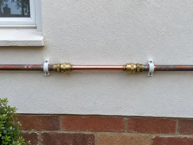 Repaired copper water pipe on an exterior rendered wall above a brick base in Parklea